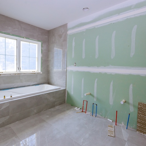 A large bathroom in the middle of a remodel. The bath area has stone siding but the rest of the walls are bare.