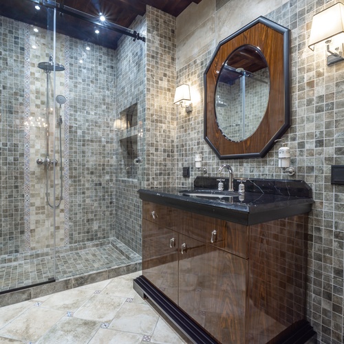 A modern bathroom with a glass walk-in shower, tiled walls, dark wood vanity, black countertop, and framed wall mirror.