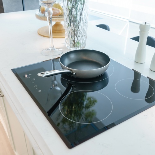 A frying pan resting on a black induction stove with three burners on a kitchen island with a white countertop.