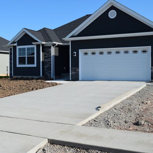 A newly built home with a concrete driveway. Instead of a grass lawn, there is newly placed dirt in front of it.