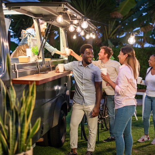 A group of employees at an outdoor company event. They gather around a rented bar trailer with patio lights.