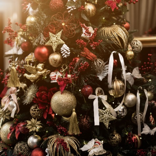 A Christmas tree covered in red and gold ornaments, glittering stars, red berries, white ribbons, and gold bows.