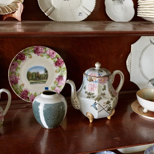 Vintage dishes, a vintage teapot, and a vintage saucer with floral patterns sit on a cabinet that's a dark cherry color.
